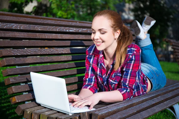 Εφηβικό κορίτσι που βρίσκεται στον πάγκο με το laptop στο πάρκο — Φωτογραφία Αρχείου