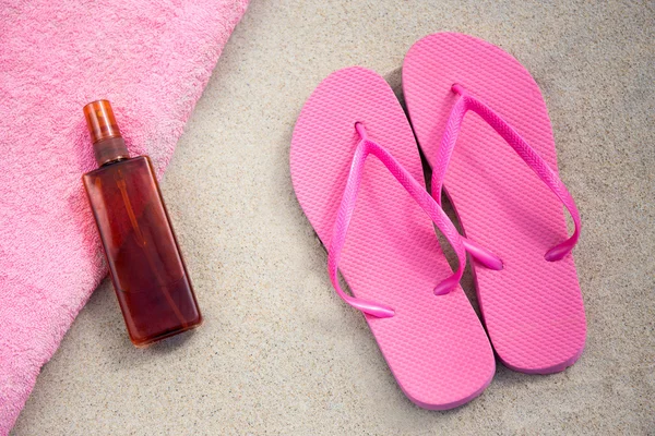 Chanclas rosa y botella de la loción de bronceado en la playa — Foto de Stock