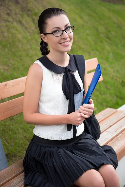 Portrait of beautiful school girl or student sitting on bench in — Stock Photo, Image