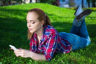 mutlu genç kız parkta çim akıllı telefon ile yalan