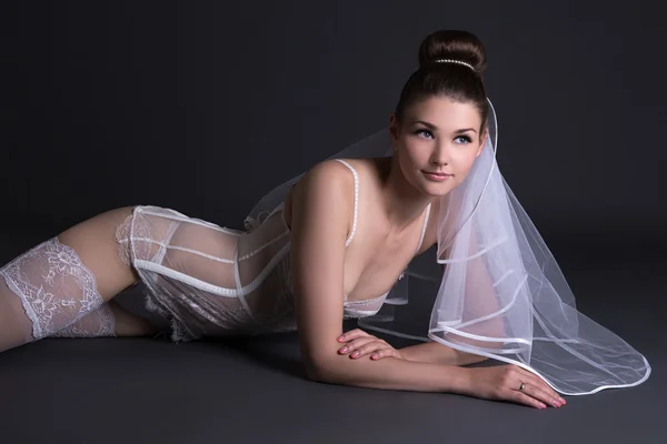 Noiva linda em lingerie sexy branco com véu mentindo sobre cinza — Fotografia de Stock