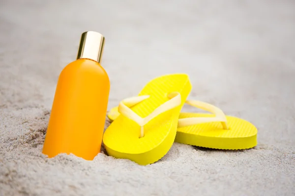 Concepto del verano - zapatillas y botella de la loción de bronceado en la playa de arena — Foto de Stock