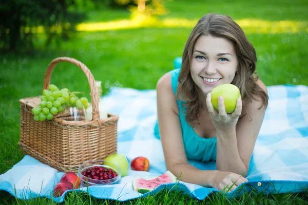 Jonge mooie vrouw met picknickmand en vruchten in tuin — Stockfoto