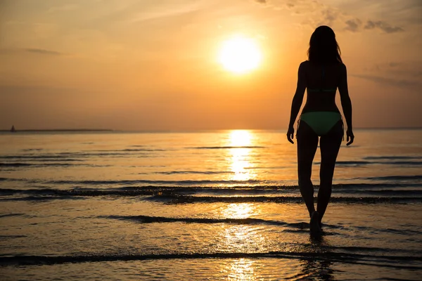 Silhouette de jeune femme en bikini, marchant sur la plage au coucher du soleil — Photo