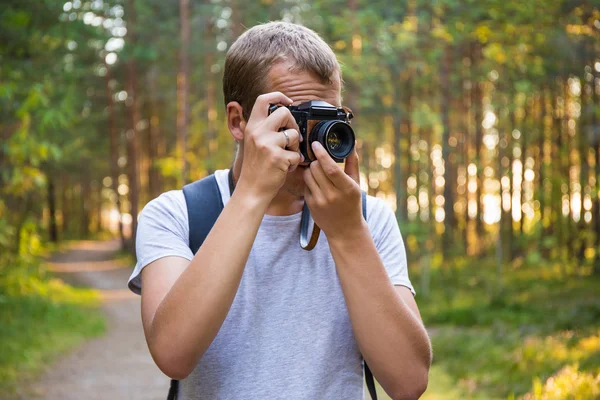 Man med ryggsäcken ta ett foto med retro kamera i skogen — Stockfoto