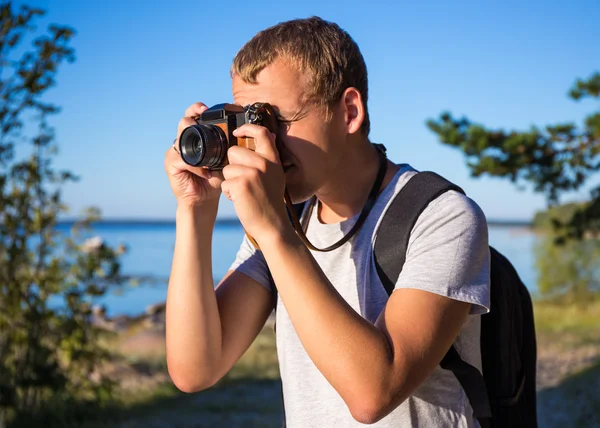 Człowiek z plecaka robienia zdjęcia aparatem retro na plaży — Zdjęcie stockowe