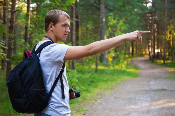 Young man with backpack showing on something in forest — Stock Photo, Image