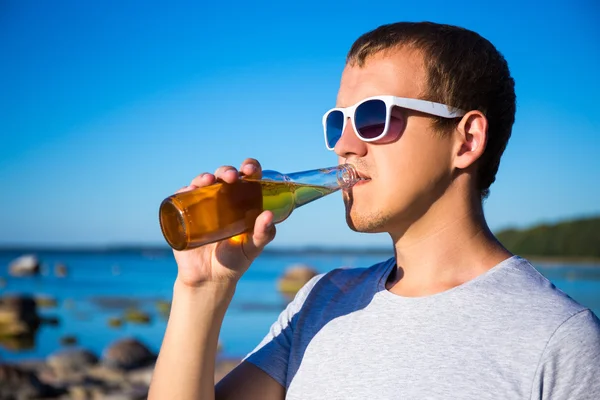 Concetto di estate - uomo bello bere birra sulla spiaggia — Foto Stock