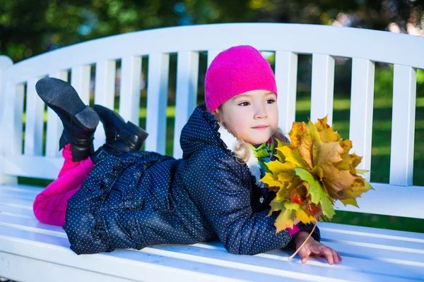 Menina bonita, deitado no banco com maple folhas no parque — Fotografia de Stock