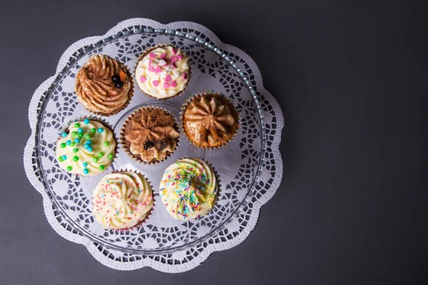 Close-up de doces cupcakes coloridos na placa de vidro sobre cinza — Fotografia de Stock
