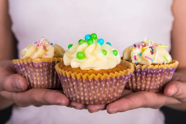Três bolinhos coloridos doces com creme de manteiga em mãos femininas — Fotografia de Stock