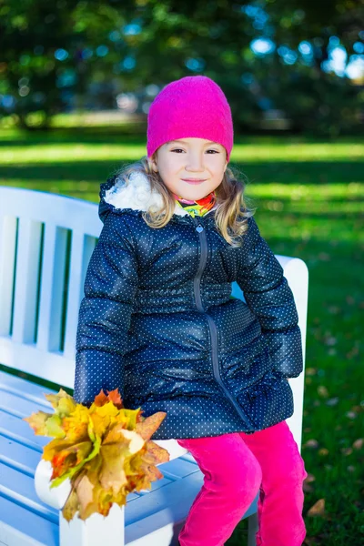 Schönes Mädchen sitzen auf der Bank mit Ahorn Blätter im park — Stockfoto