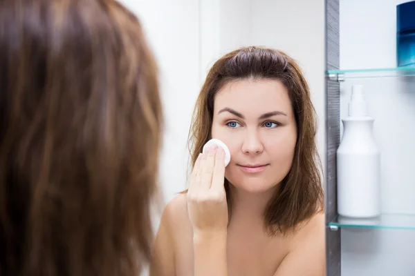 Ung kvinna tvätta hennes ansikte med lotion i badrum — Stockfoto