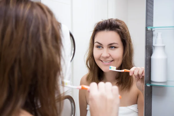 Unga vackra kvinnan borsta tänderna och tittar på spegel i ba — Stockfoto