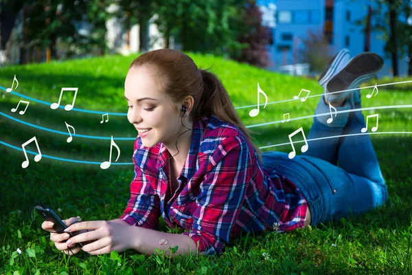 Teenage girl lying and listening music with smart phone in park — Stock Photo, Image