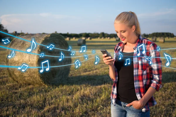 beautiful blonde woman listening music with smart phone in field