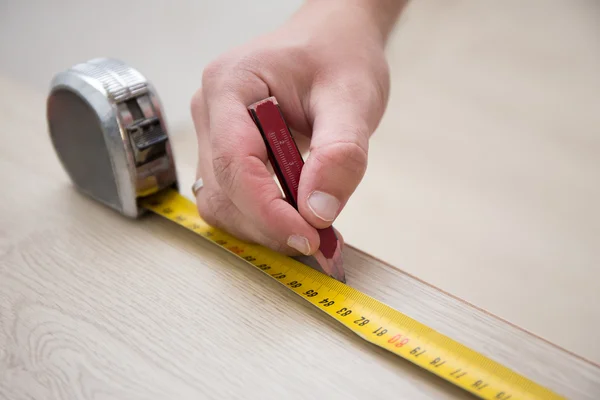 Erkek teyp ölçme ile eller ve yeni lamine ahşap zemin — Stok fotoğraf