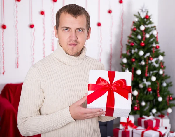 Young man holding christmas present box in decorated room — Stock Photo, Image