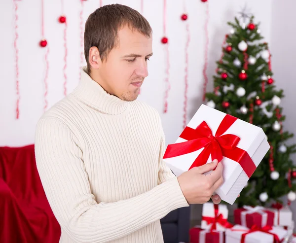 Young man opening christmas present box in decorated room — Stock Photo, Image