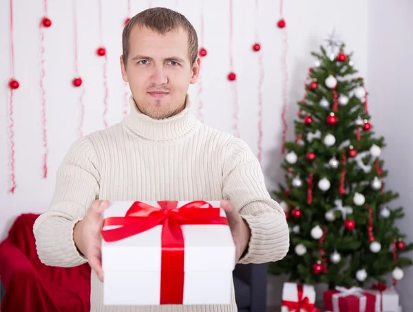 Young man giving christmas present box over christmas background — Stock Photo, Image