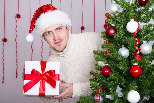 Handsome man in santa hat with gift box and decorated Christmas — Stock Photo, Image