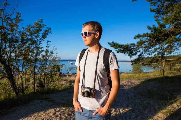 Handsome man with backpack and retro camera on the beach — Stock Photo, Image