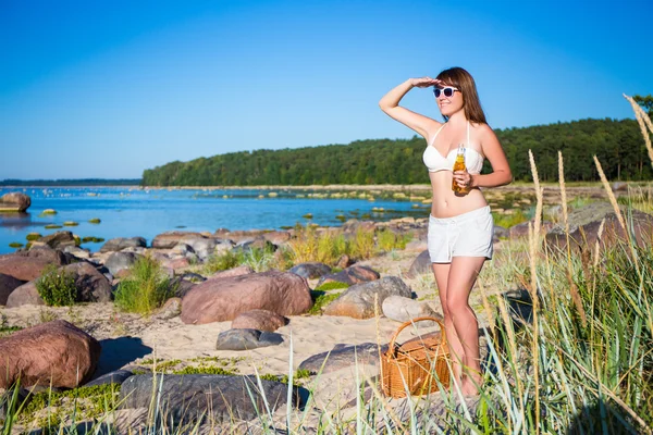 Beautiful woman with beer and picnic basket posing on the beach — Stock Photo, Image