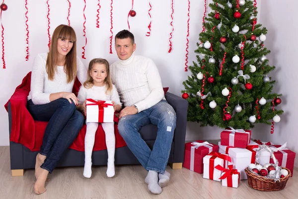 Giovane famiglia che si siede nel salone decorato con tre di Natale — Foto Stock