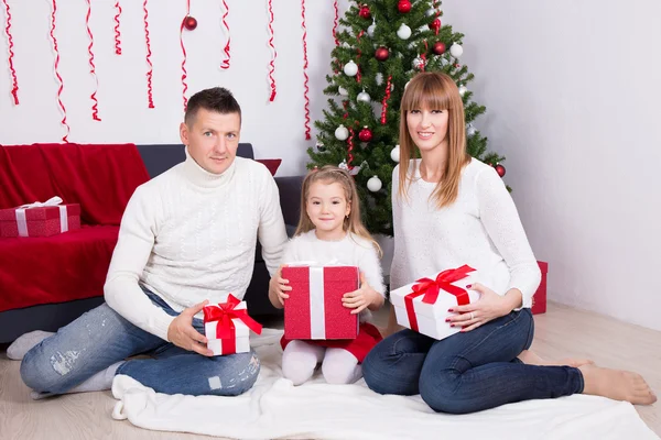 Familia joven sentado con regalo cajas frente a árbol de Navidad —  Fotos de Stock