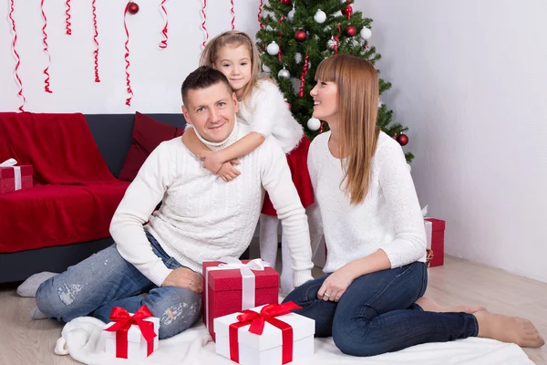 Ung familj med gåva lådor framför granen — Stockfoto