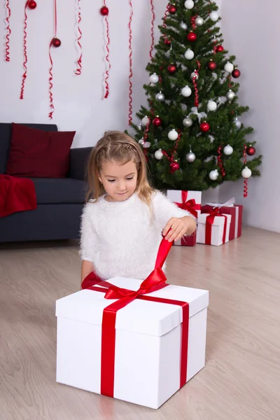 집에서 크리스마스 트리 근처 큰 선물 상자를 열고 어린 소녀 — 스톡 사진