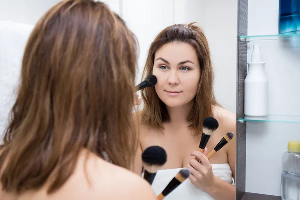 Mujer mirando al espejo y aplicar el maquillaje en el baño —  Fotos de Stock