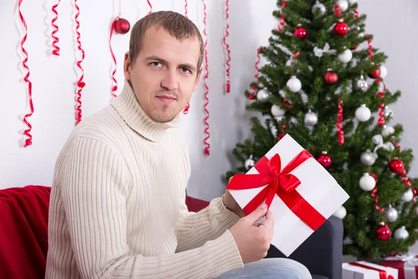 Glad ung vacker man öppnar julklapp i vardagsrum — Stockfoto