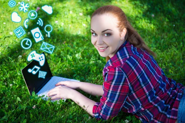 Teenage girl lying on grass in park and using laptop with differ — Stock Photo, Image