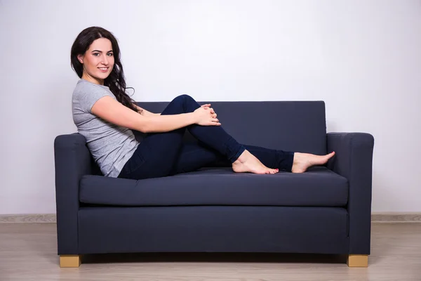 Bela jovem feliz sentado no sofá em casa — Fotografia de Stock