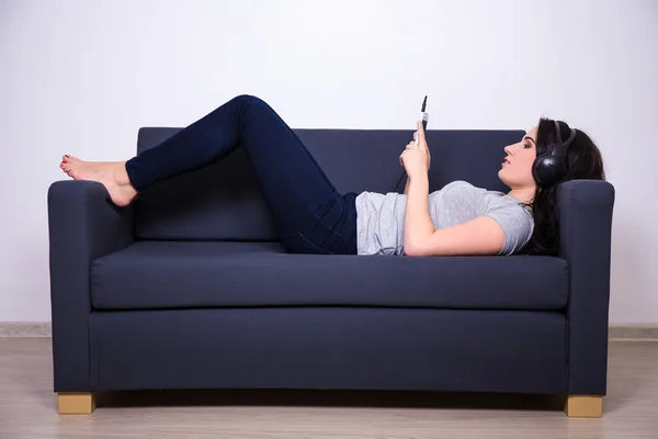 Boldog asszony feküdt a kanapén, és zene-val mozgatható telefon — Stock Fotó