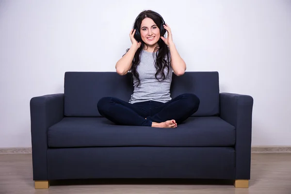 Happy woman sitting on sofa and listening music with headphones — Stock Photo, Image