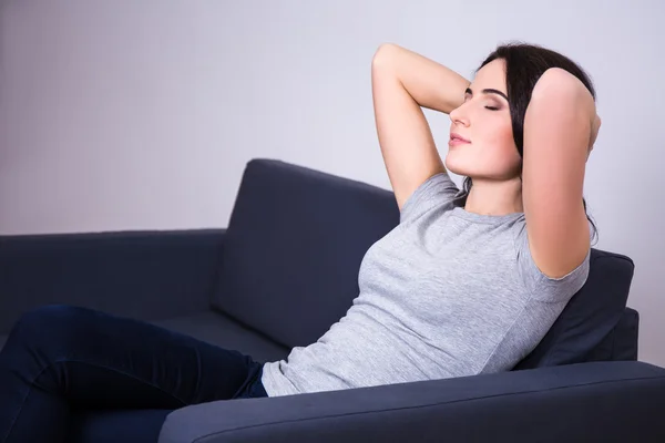 Smiling young woman lying on sofa at home — Stock Photo, Image
