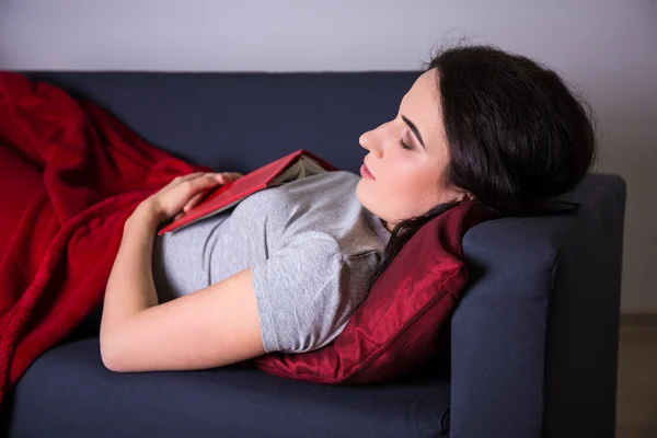 Jeune femme dormant avec livre sur canapé à la maison — Photo