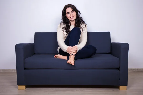 Young woman sitting on sofa at home — Stock Photo, Image