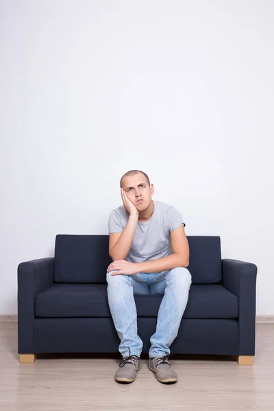Idea koncepce - přemýšlivý muž sedí na pohovce přes bílou zeď — Stock fotografie