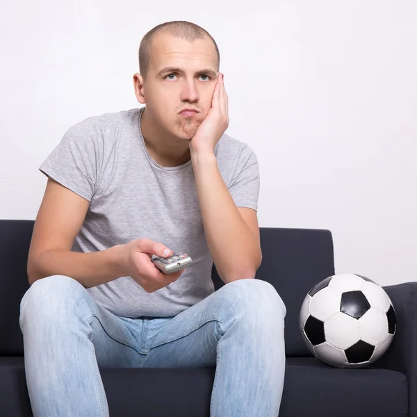 Znudzony wentylator z piłką, oglądając mecz piłki nożnej w telewizji — Zdjęcie stockowe