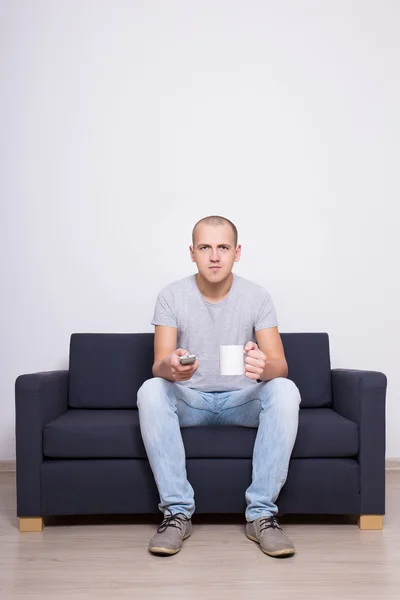 Fiatal jóképű férfi ül a kanapén, és nézi a tv t csésze — Stock Fotó