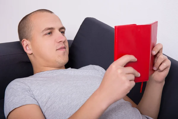 Jonge knappe man liggend op de Bank en het boek lezen — Stockfoto