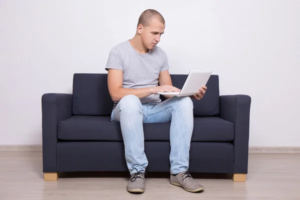 Красивый мужчина сидит на диване и с помощью ноутбука — стоковое фото