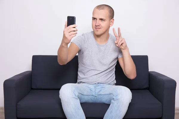若い男がソファの上に座って、モバイル ph と selfie 写真を撮る — ストック写真