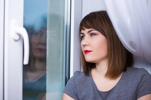 Beautiful dreaming woman sitting by the window — Stock Photo, Image