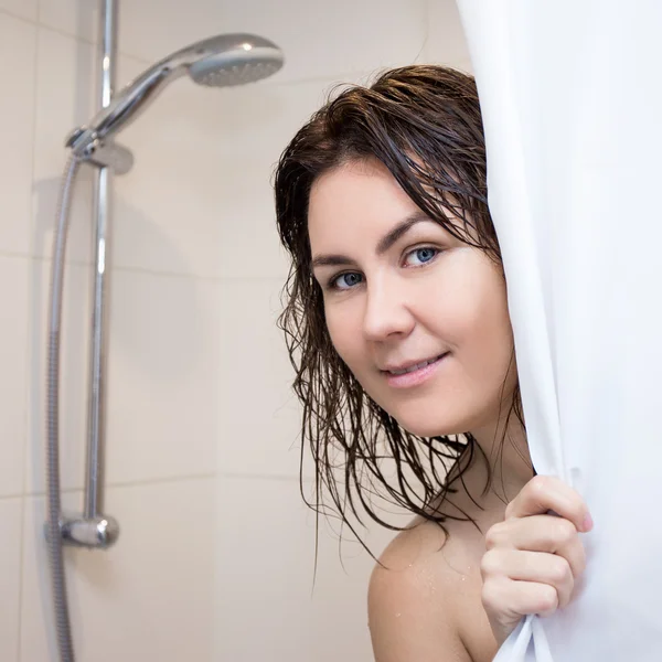 Young woman standing in shower and covering herself with curtain — Stockfoto