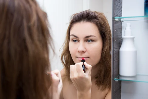 Mujer mirando al espejo y aplicar lápiz labial en el baño — Foto de Stock