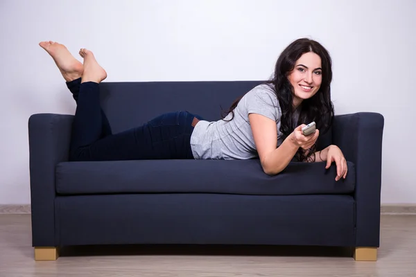 Щаслива жінка лежить на дивані і дивиться телевізор вдома — стокове фото